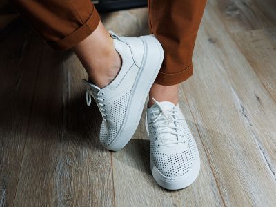 Close-up of female legs in white perforated leather sneakers. Women's summer sneakers. Collection of women's leather shoes